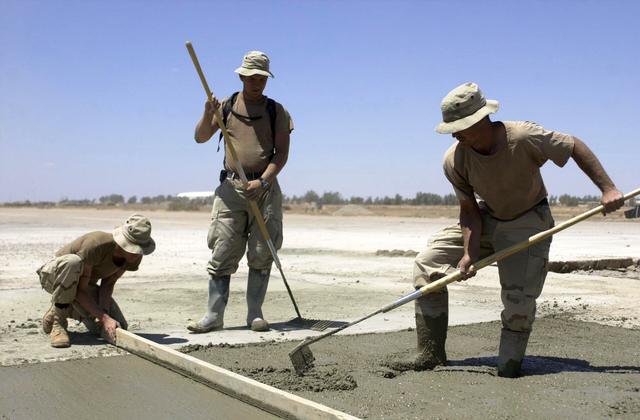 Two workers raking and screeding wet concrete