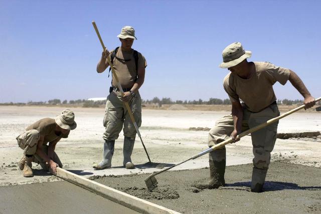Two workers raking and screeding wet concrete