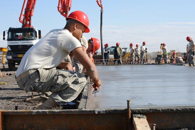 Concreter kneeling to finish a freshly poured slab with workers in the background